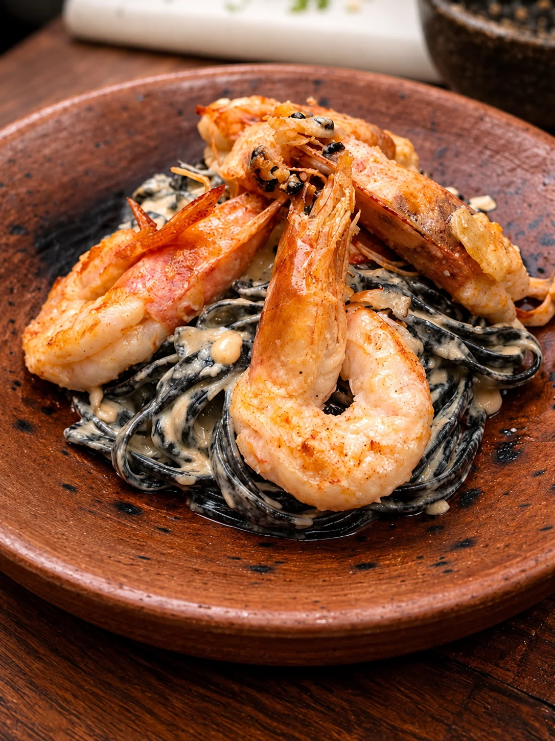 Fetuccini negro con camarones servido en un plato de barro de Dassani